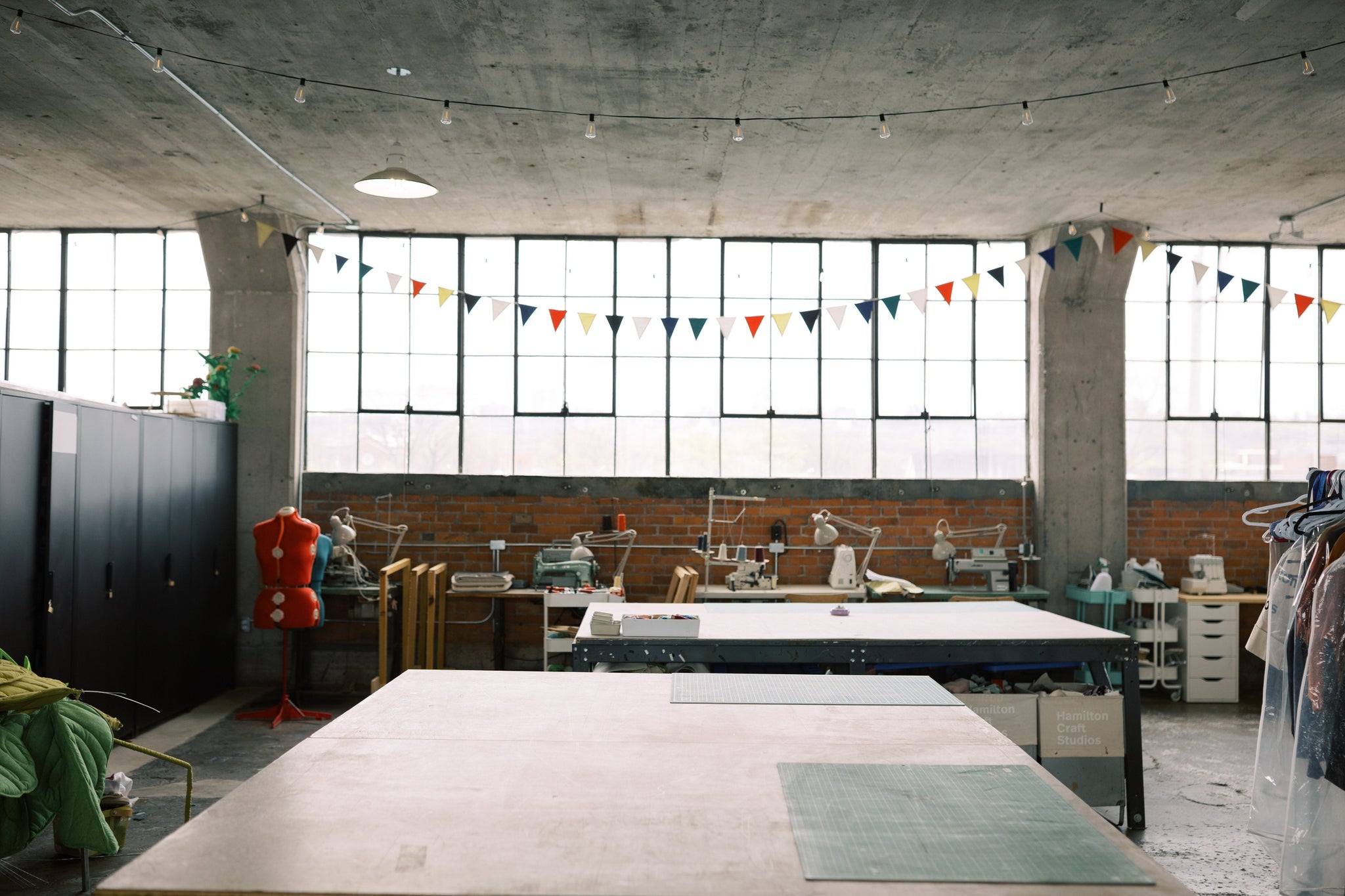large cutting tables in a community sewing studio with large industrial warehouse windows in the background