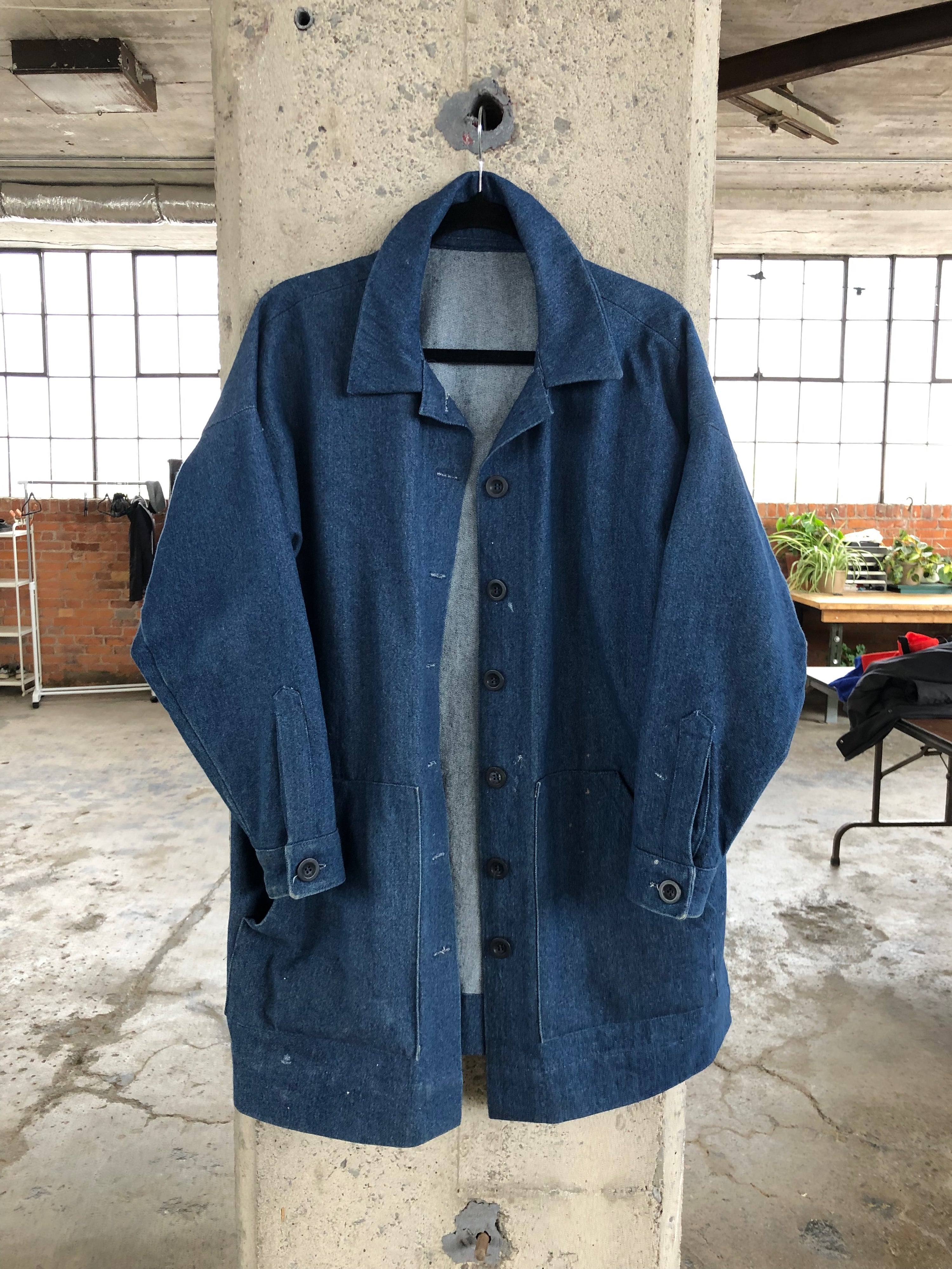 A denim chore coat hanging on a concrete pillar in a warehouse setting