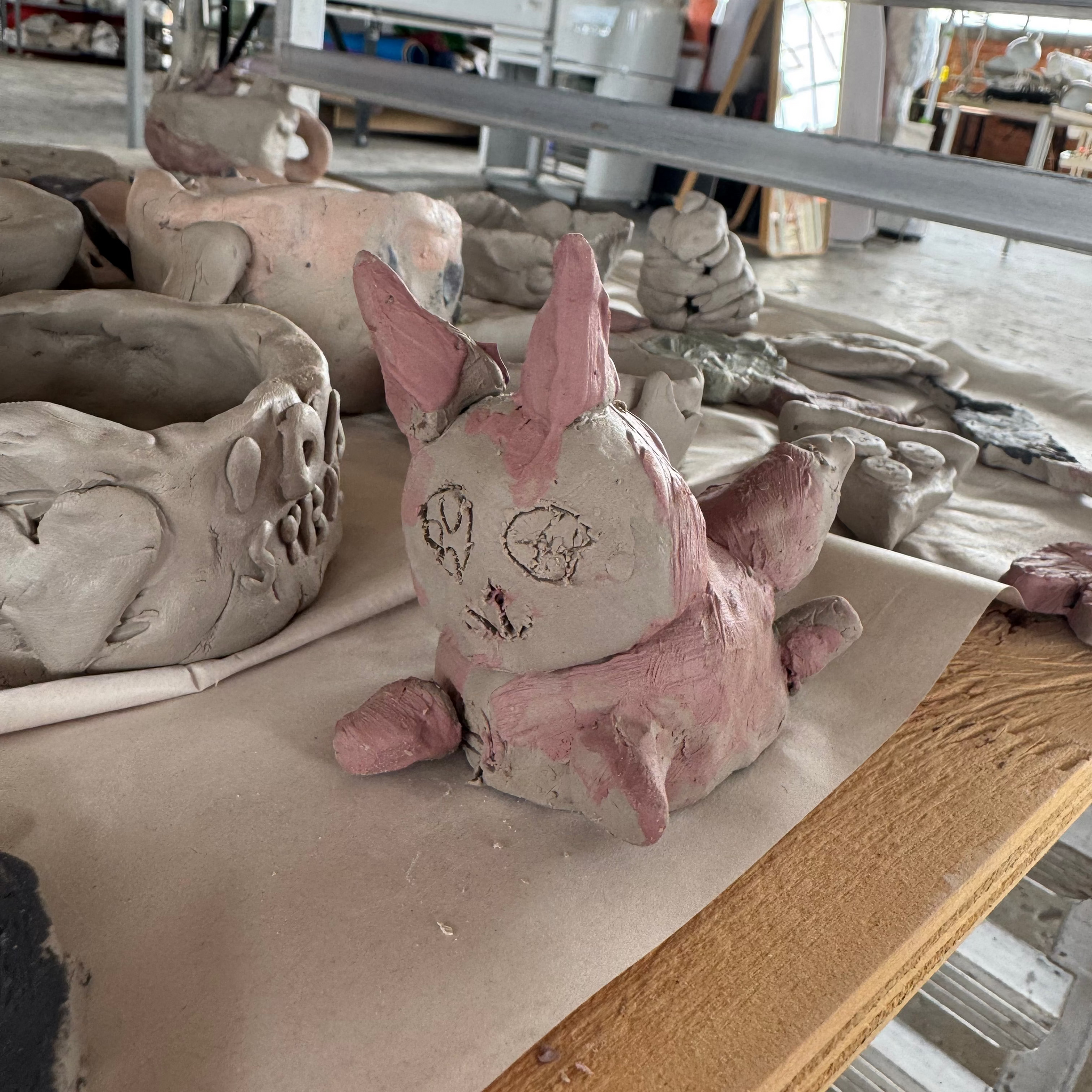 Clay sculpture of a pink creature on a workbench in a pottery studio