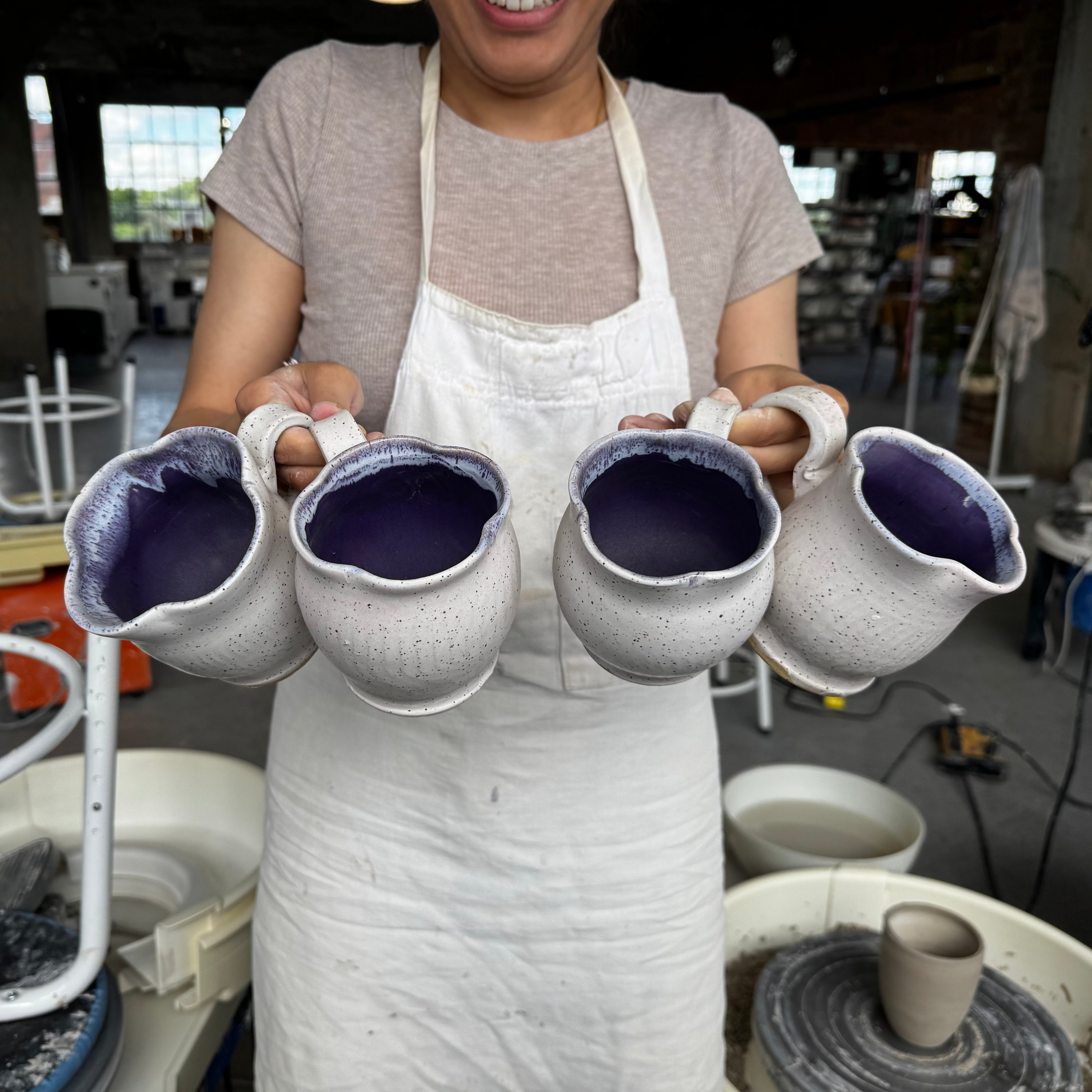 Person holding four ceramic cups with a workshop background