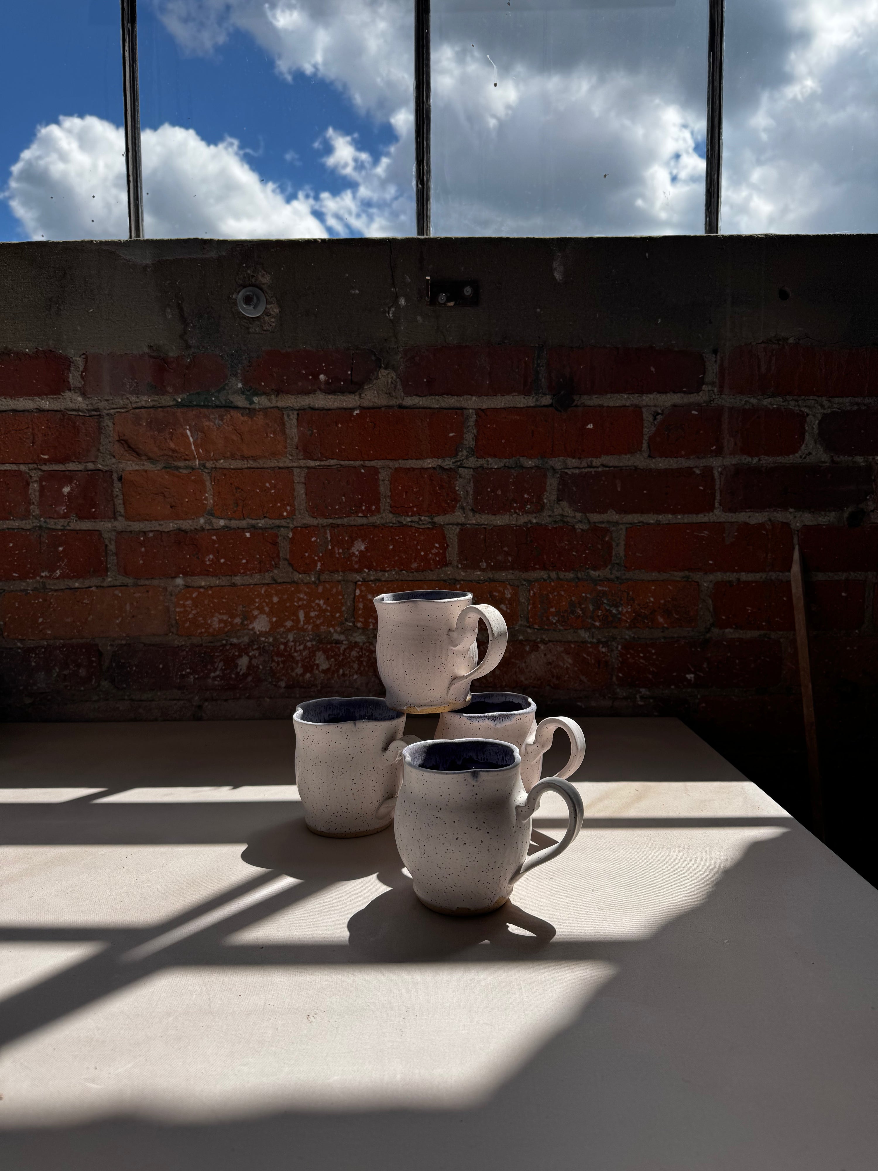 four ceramic mugs on a table with a brick wall and blue sky in the background